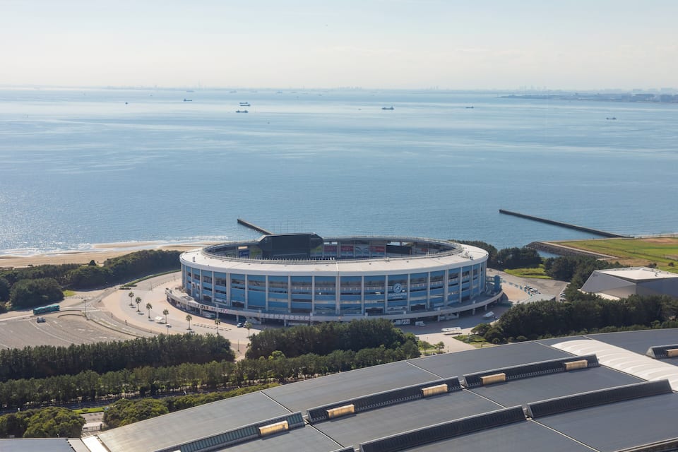 Um estádio circular grande com um parque de estacionamento, rodeado por uma praia e um corpo de água.