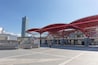 A modern architectural structure with a red metal framework and a tall skyscraper in the background.
