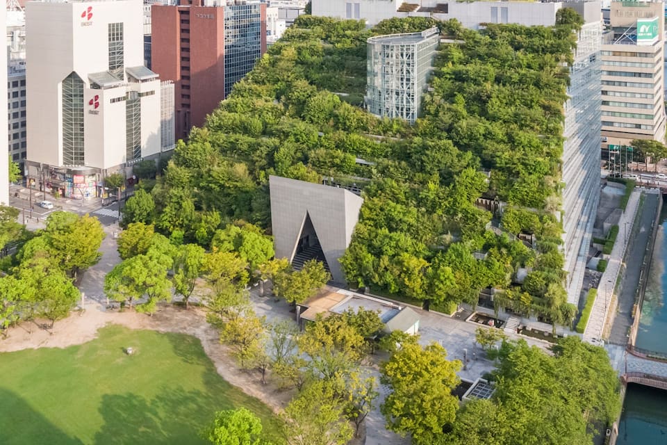 Een stadsgezicht met een opvallend gebouw met een uniek, driehoekig ontwerp, omringd door weelderige groene beplanting.