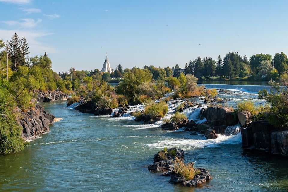 Un río con orillas rocosas, árboles y una torre distante.