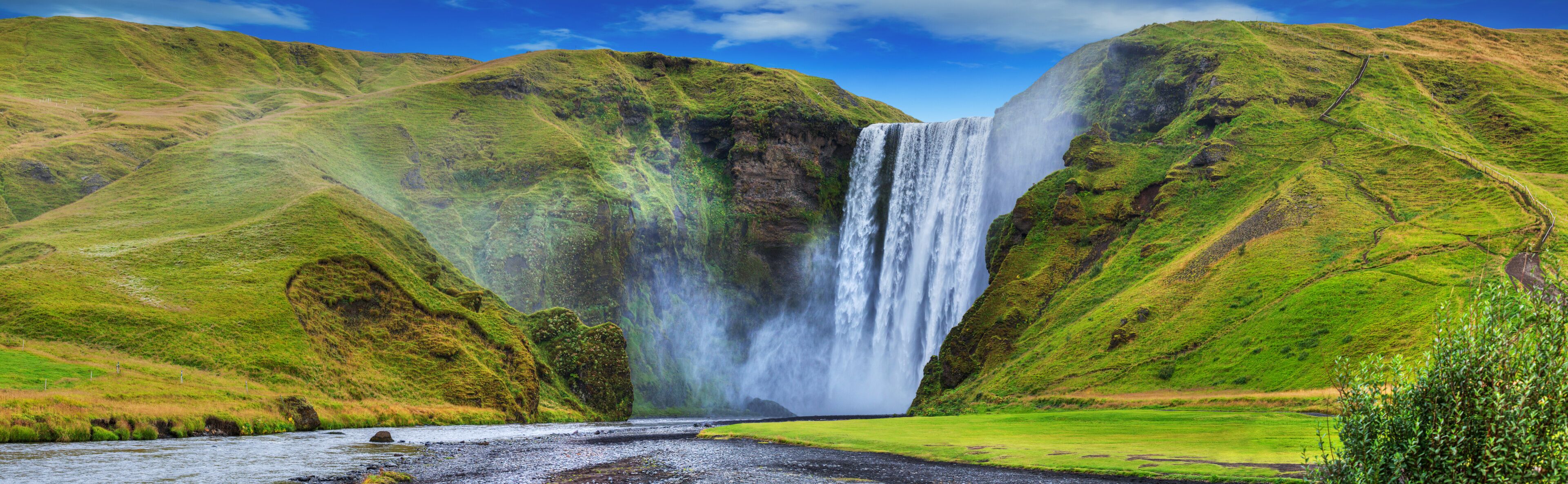 A waterfall cascading down a steep cliff surrounded by lush green hills.