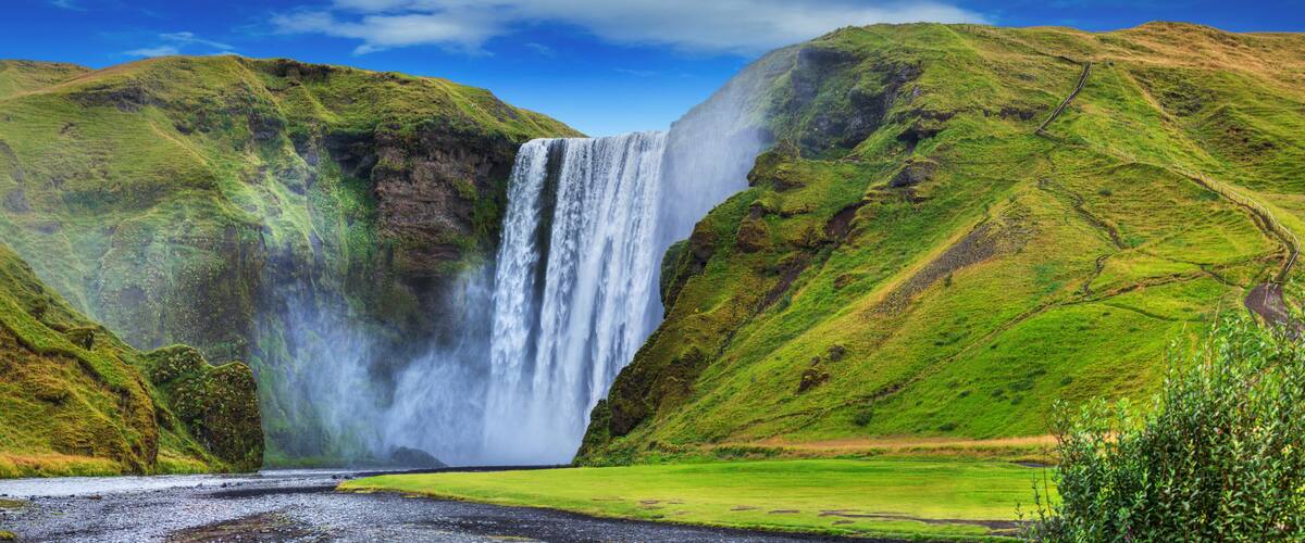A waterfall cascading down a steep cliff surrounded by lush green hills.