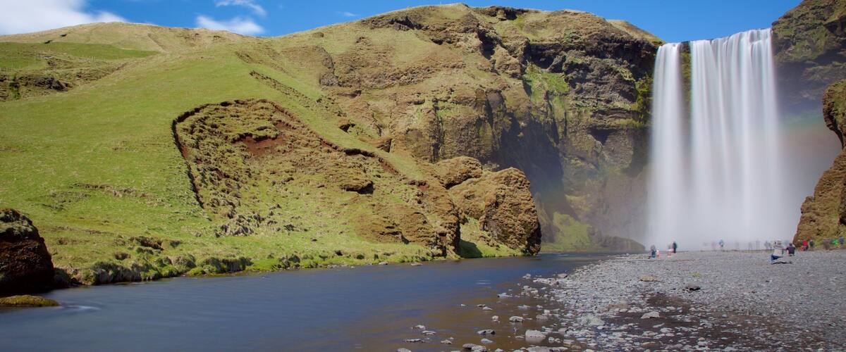 A waterfall cascading down a rocky cliff into a river, surrounded by green hills.