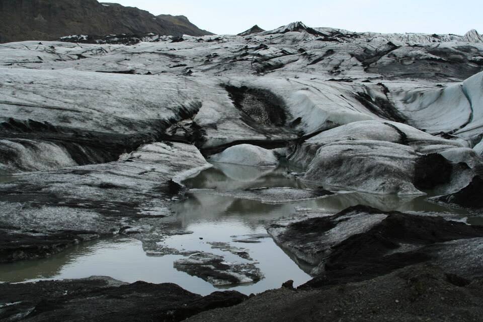 A glacier with crevasses and a small body of water.