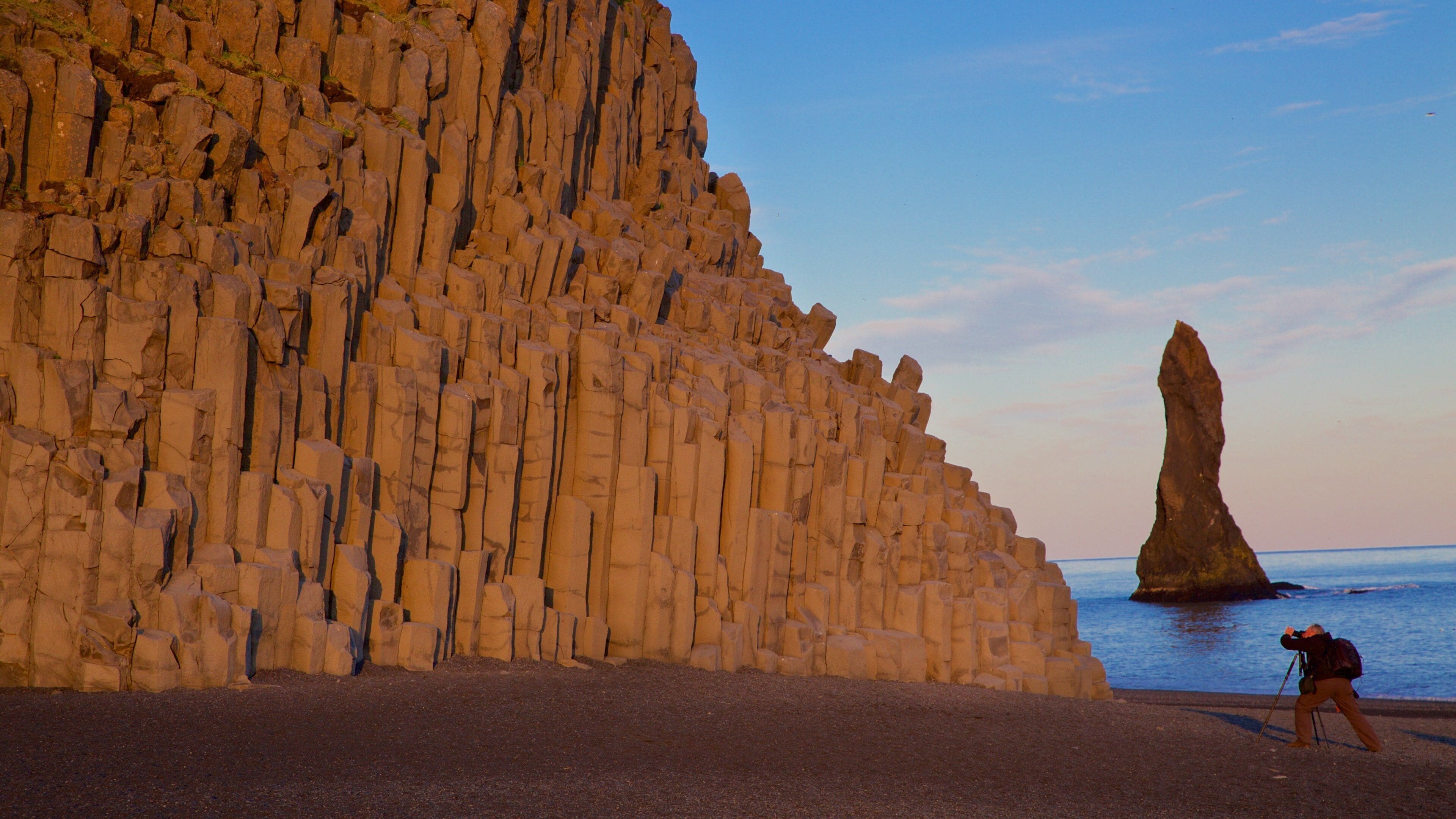 A rocky cliff with a tall, narrow rock formation in the sea.