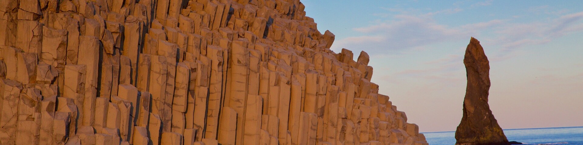 A rocky cliff with a tall, narrow rock formation in the sea.
