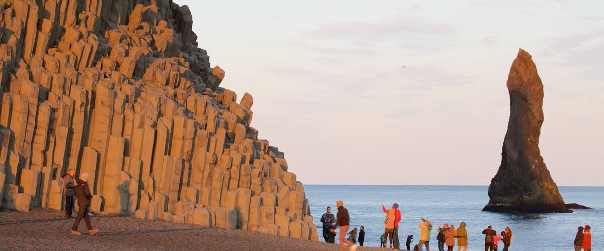 Reynisdrangar featuring general coastal views and a sunset as well as a large group of people