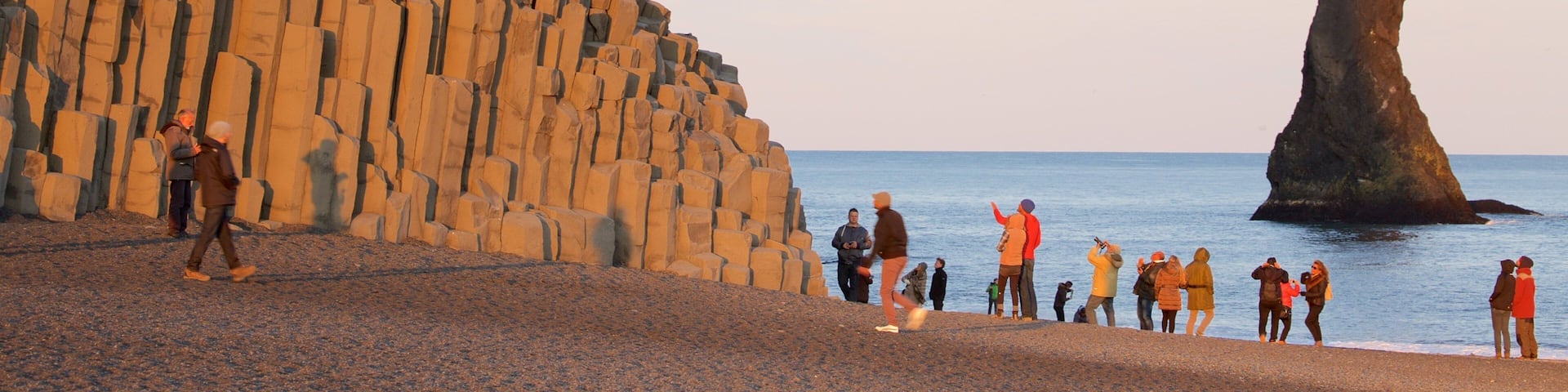 Reynisdrangar featuring general coastal views and a sunset as well as a large group of people