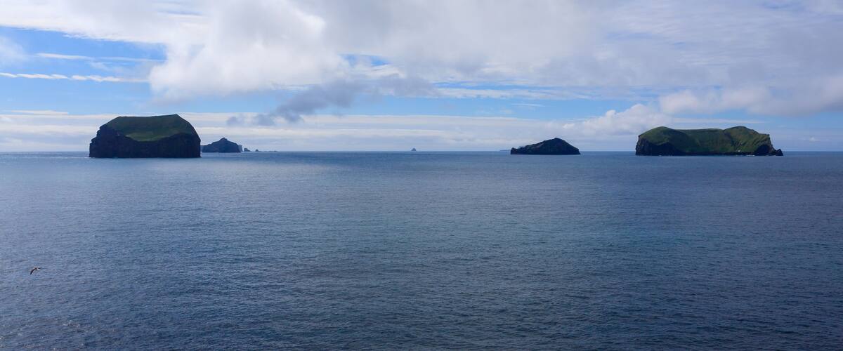 A calm sea with two green islands and a distant rocky outcrop.