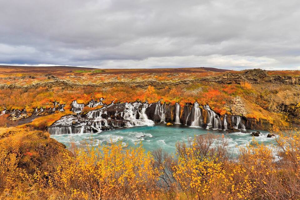 Una cascada que aboca a una bassa de color turquesa envoltada de fullatge daurat i vermell.
