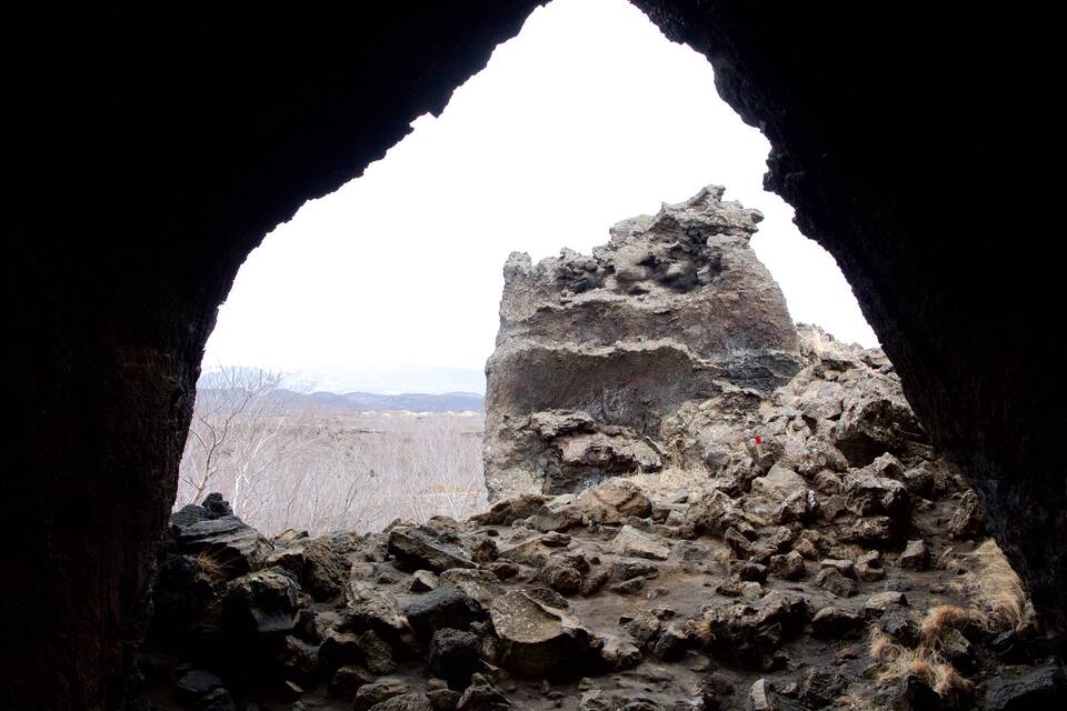 Ruínas rochosas visíveis através da entrada de uma caverna, com paisagem nevada ao fundo.