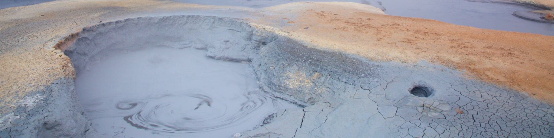 A geothermal area with a wooden viewing platform overlooking a series of hot springs and steam vents.