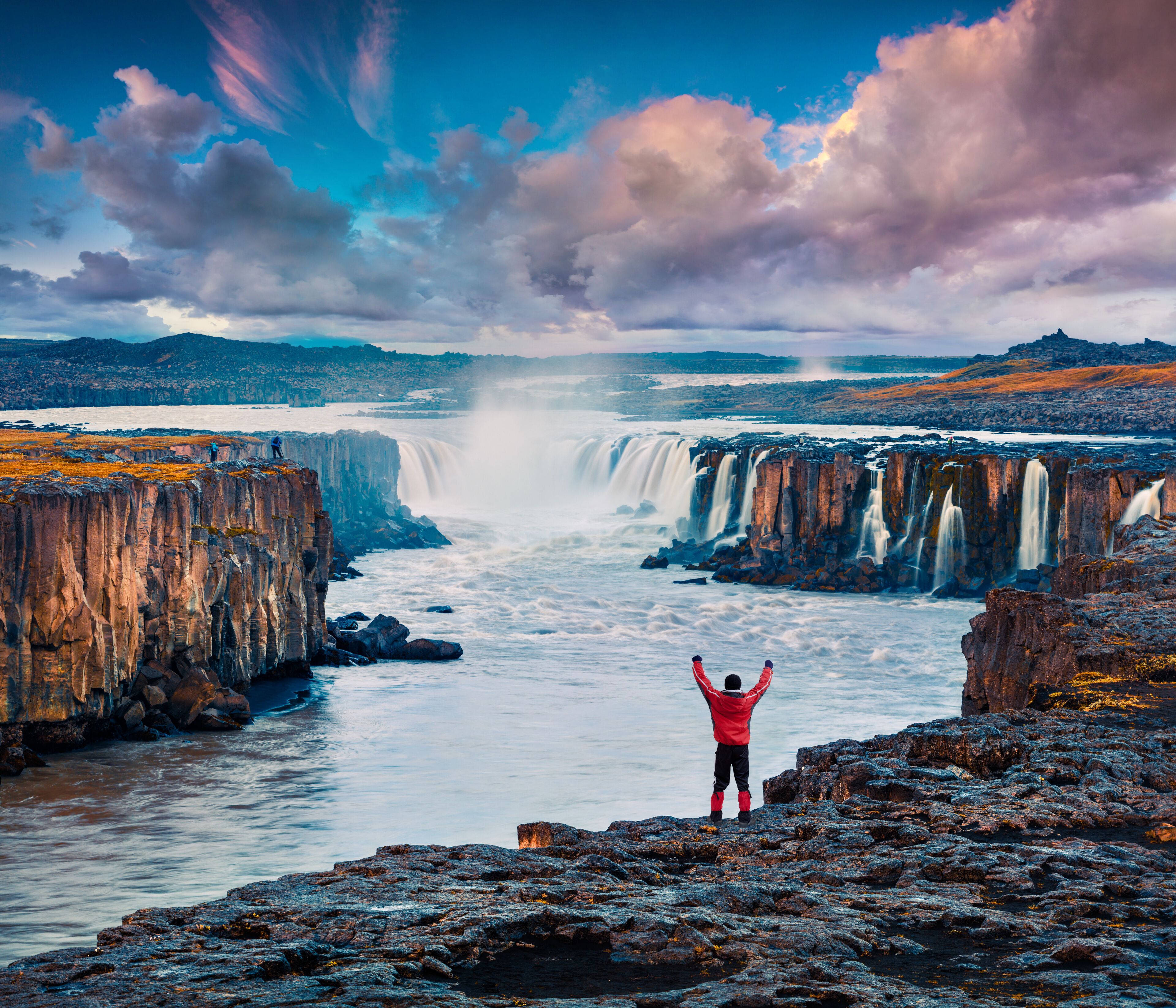 Tourist standing on the standing on the edge of Jokulsa a Fjollum river with raised hands and enjoying sunrise