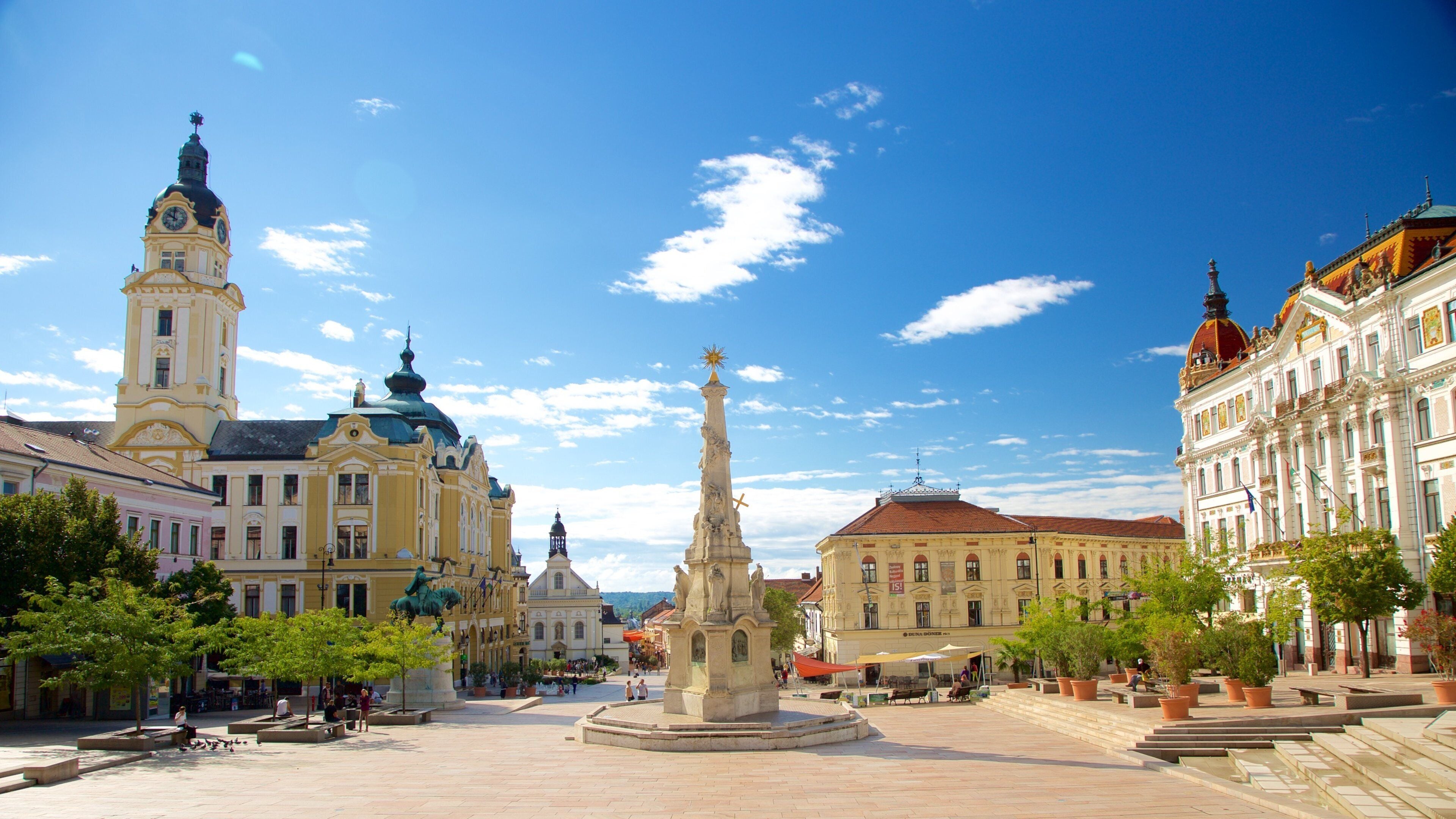 A historic square with a prominent statue, a church with a clock tower, and classical architecture.