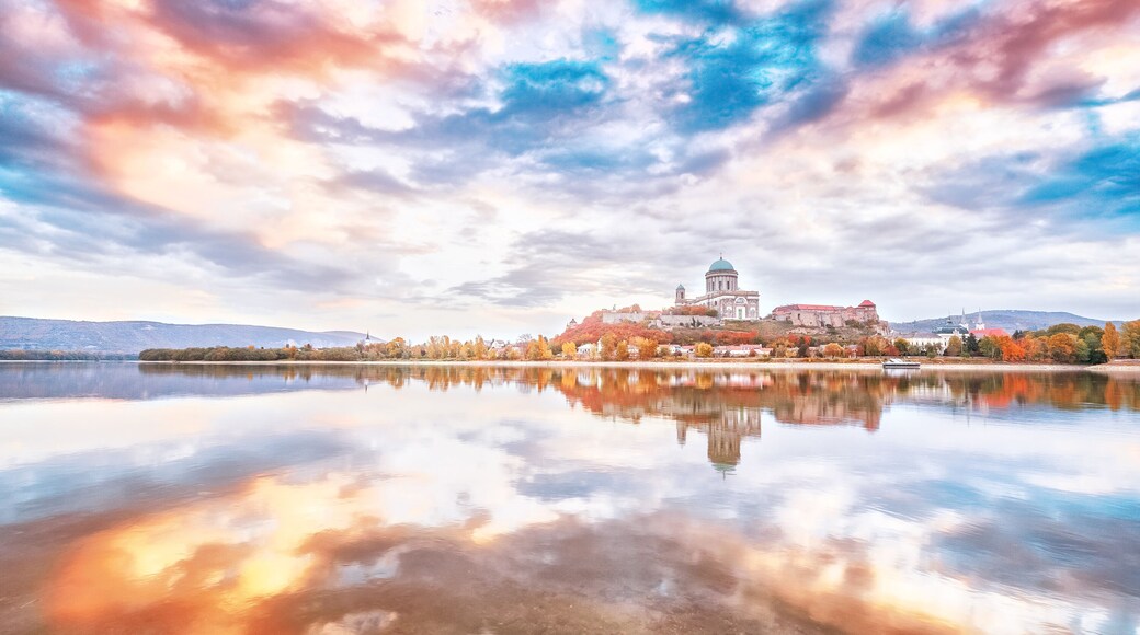 Esztergom, Hungary - view over Danube river from Sturovo, Slovakia. Epic sunrise landscape with dramatic sky of famous Basilica Esztergom. Amazing reflections of clouds. Red and blue colors scenery.