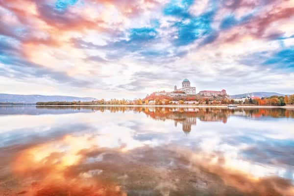 Esztergom, Hungary - view over Danube river from Sturovo, Slovakia. Epic sunrise landscape with dramatic sky of famous Basilica Esztergom. Amazing reflections of clouds. Red and blue colors scenery.