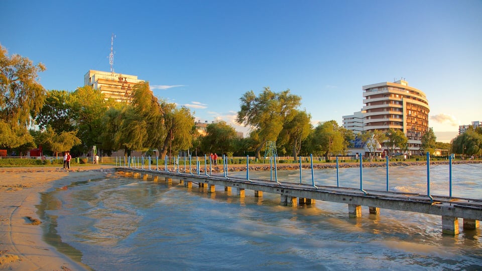 A riverside walkway with a bridge, trees, and buildings in the background.