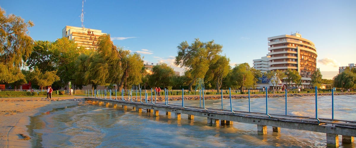 A riverside walkway with a bridge, trees, and buildings in the background.