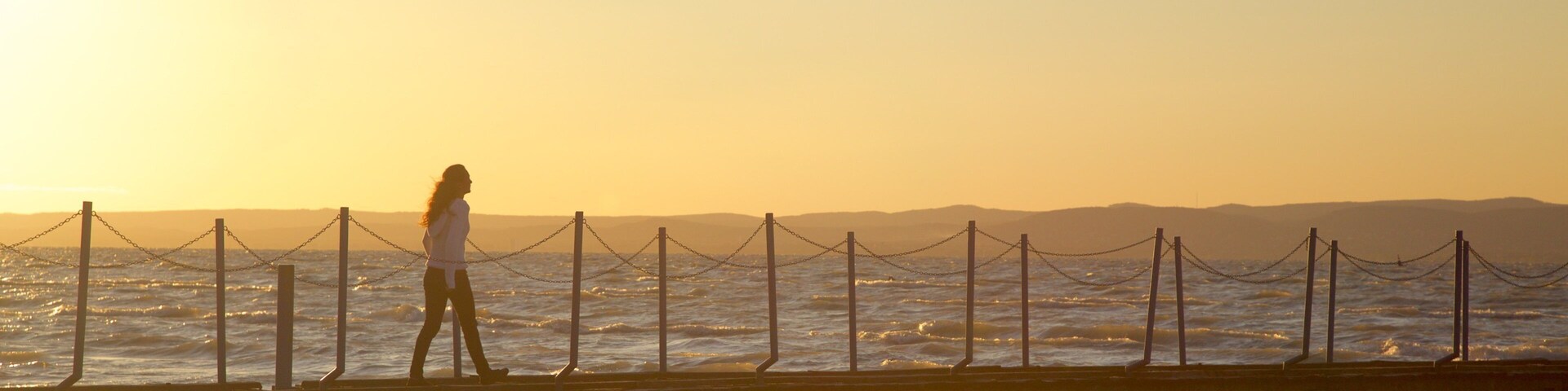 Una persona caminando sobre un muelle al atardecer.