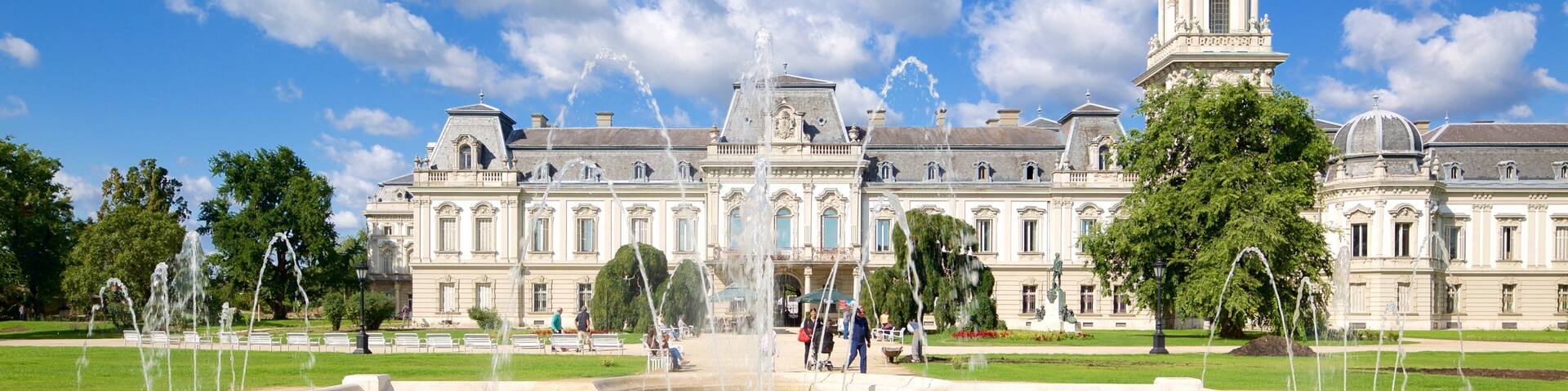 A grand building with a fountain in the foreground and a tower in the background.
