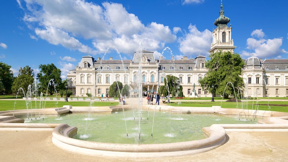 A grand building with a fountain in the foreground and a tower in the background.