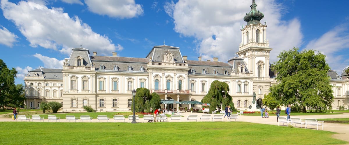 A large historic building with a prominent tower and a well-maintained garden with benches.