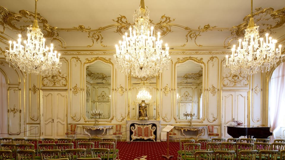 An opulent room with ornate gold detailing, large chandeliers, and a grand piano.