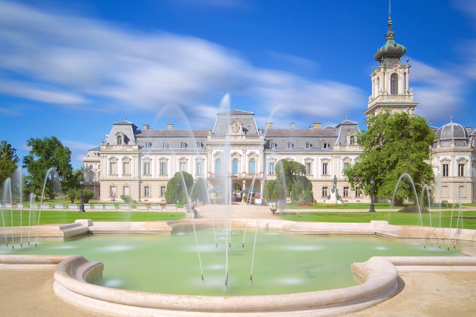 A large historic building with a fountain in the foreground.