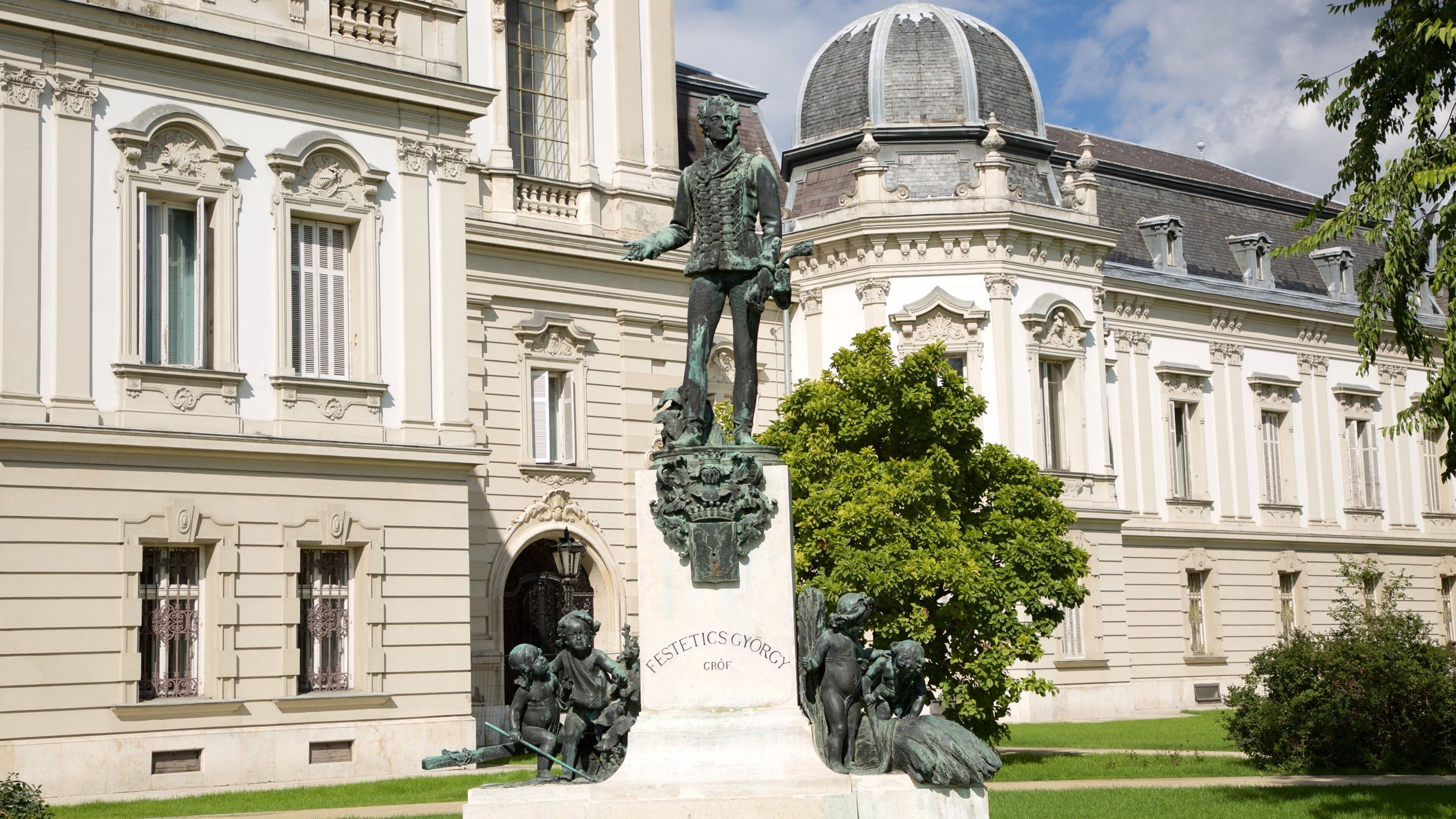 A statue of a man with a child on a pedestal in front of a large building with ornate architecture.
