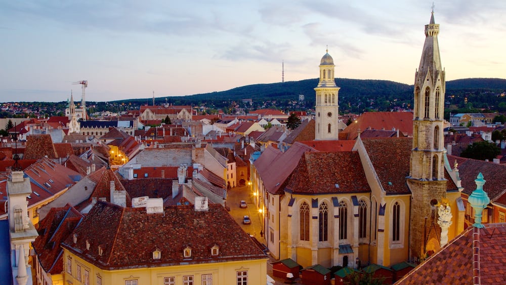 A historic town with red-tiled roofs, a prominent church with a tall spire, and a clock tower.
