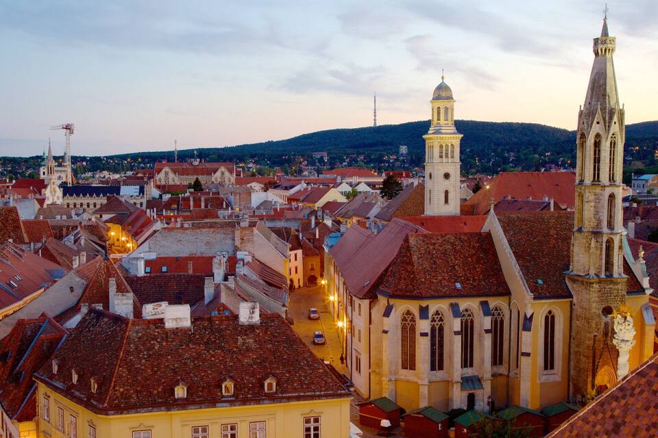 A historic town with red-tiled roofs, a prominent church with a tall spire, and a clock tower.