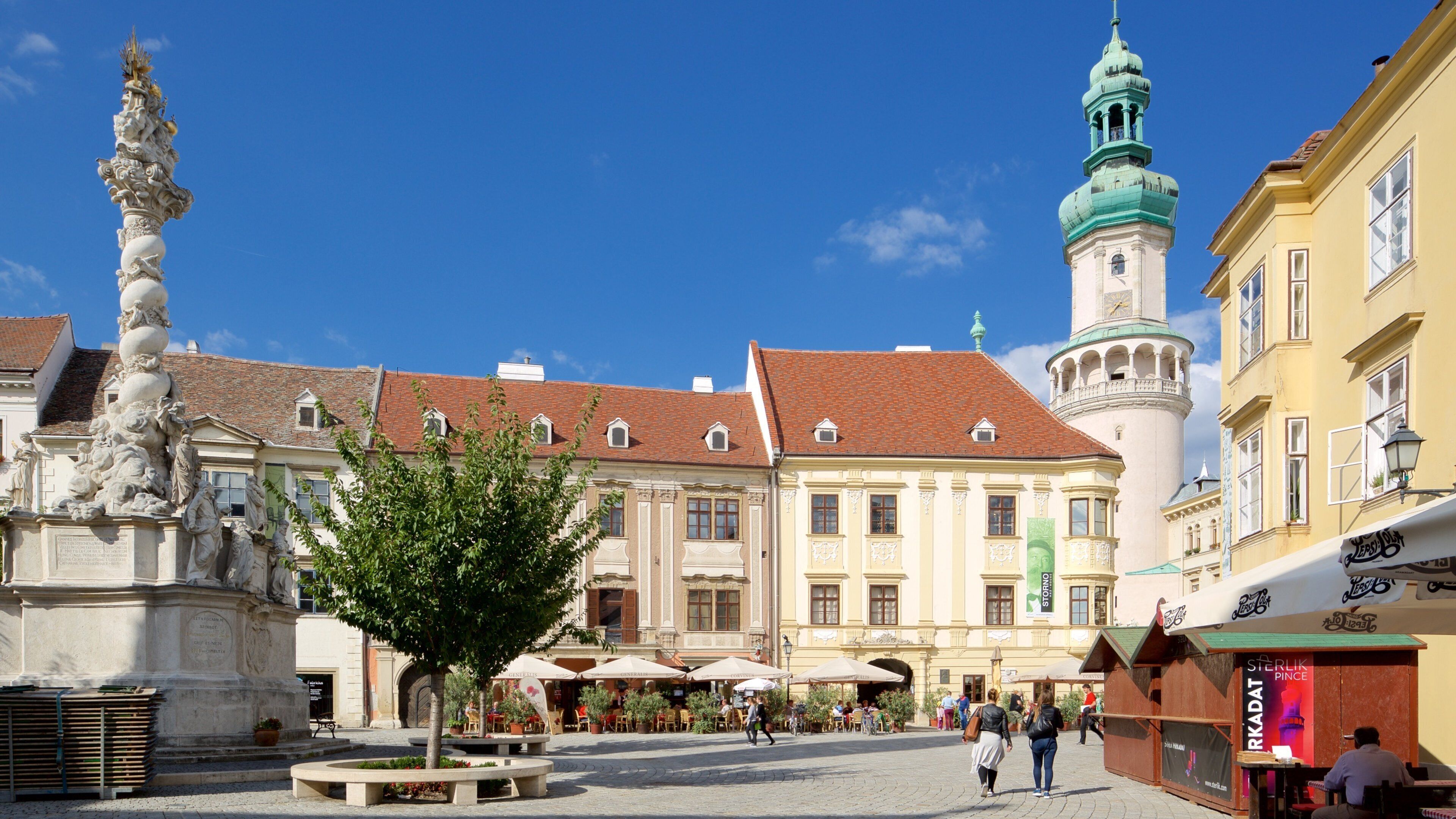 A historic square with a statue, a church tower, and traditional buildings.
