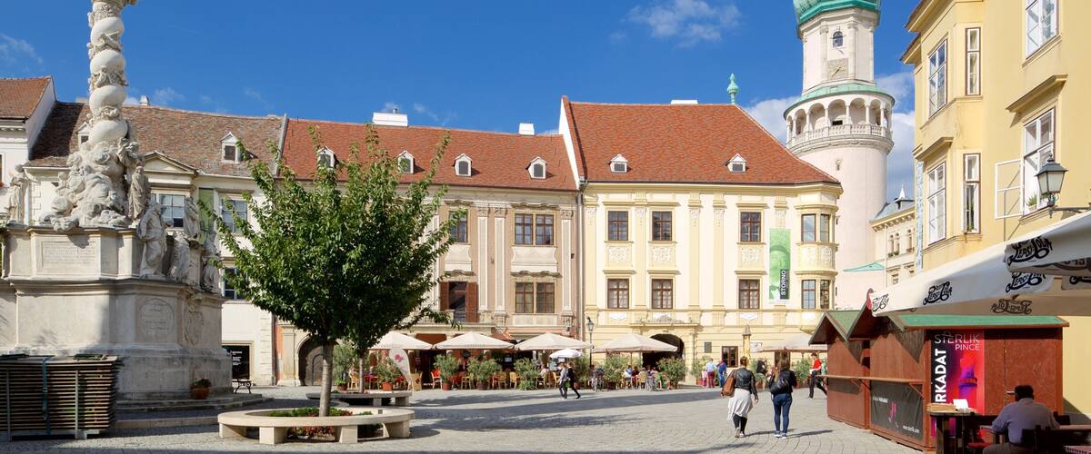 A historic square with a statue, a church tower, and traditional buildings.