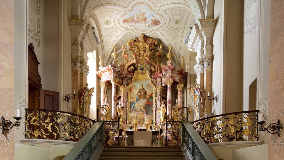 An ornate church interior with a grand altar, a staircase with golden railings, and detailed frescoes on the ceiling.