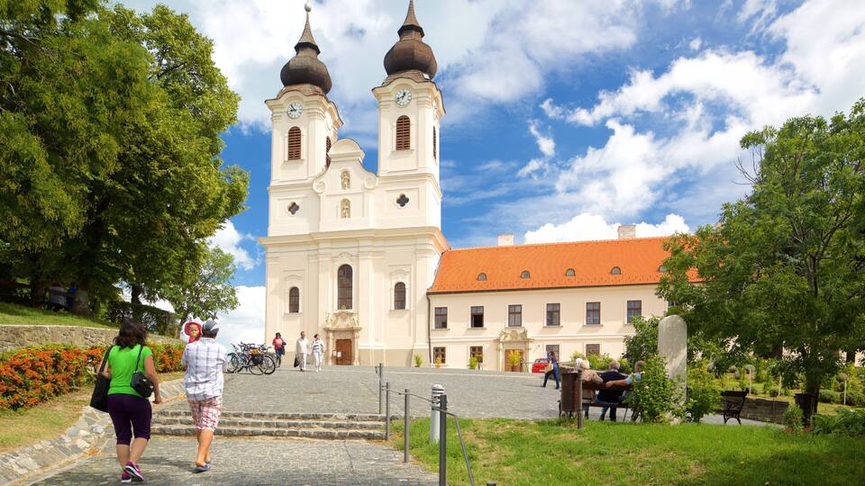 A historic church with two domes and a clock tower, surrounded by greenery and cobblestone paths.