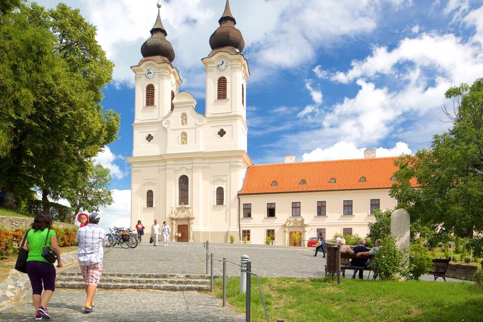 A historic church with two domes and a clock tower, surrounded by greenery and cobblestone paths.