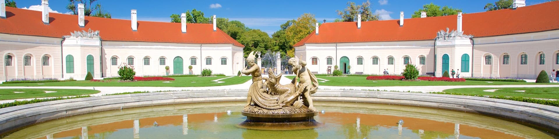 A classical fountain with statues in a formal garden, surrounded by manicured lawns and red flowers.