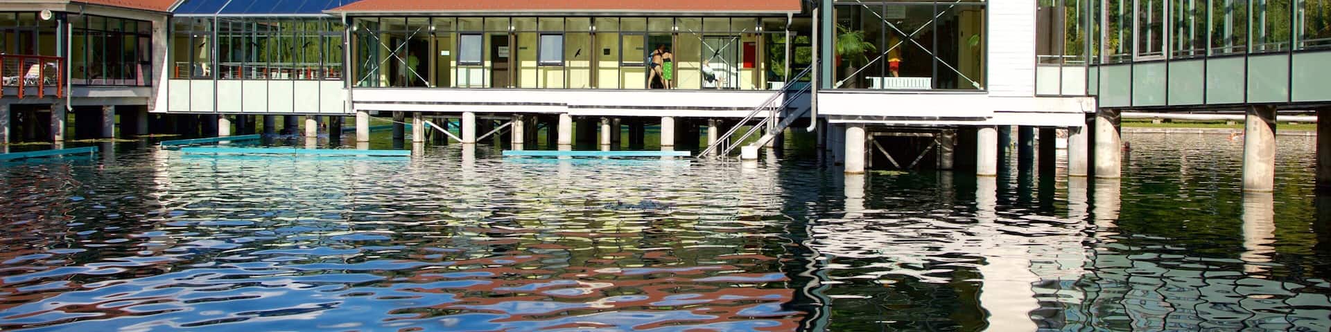 A waterfront building with a red roof, a tower, and a glass extension over the water.