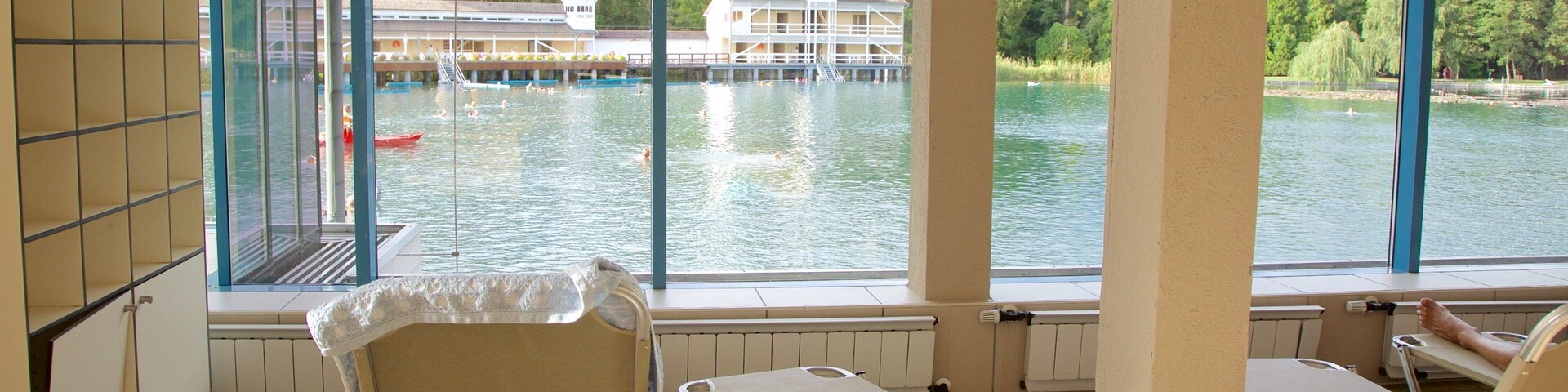 Zona junto a la piscina con sillones de descanso y vista a un lago con barcos y un edificio al fondo.