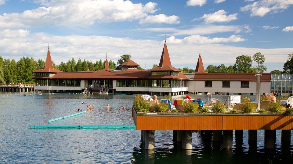 A lakeside resort with multiple buildings, a dock, and people swimming and relaxing.