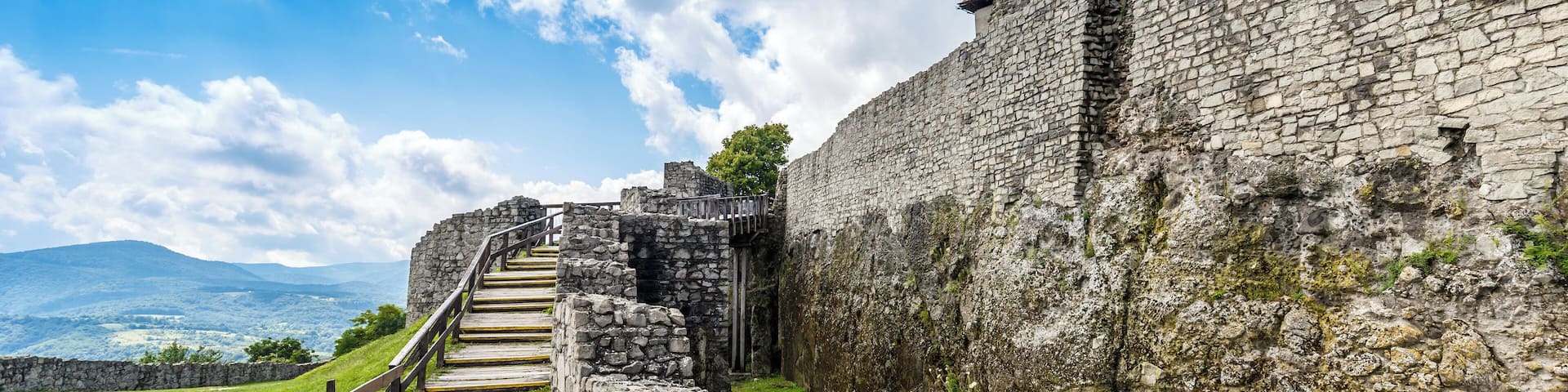 A stone staircase leading up to a historic stone wall with a clear sky and distant mountains.