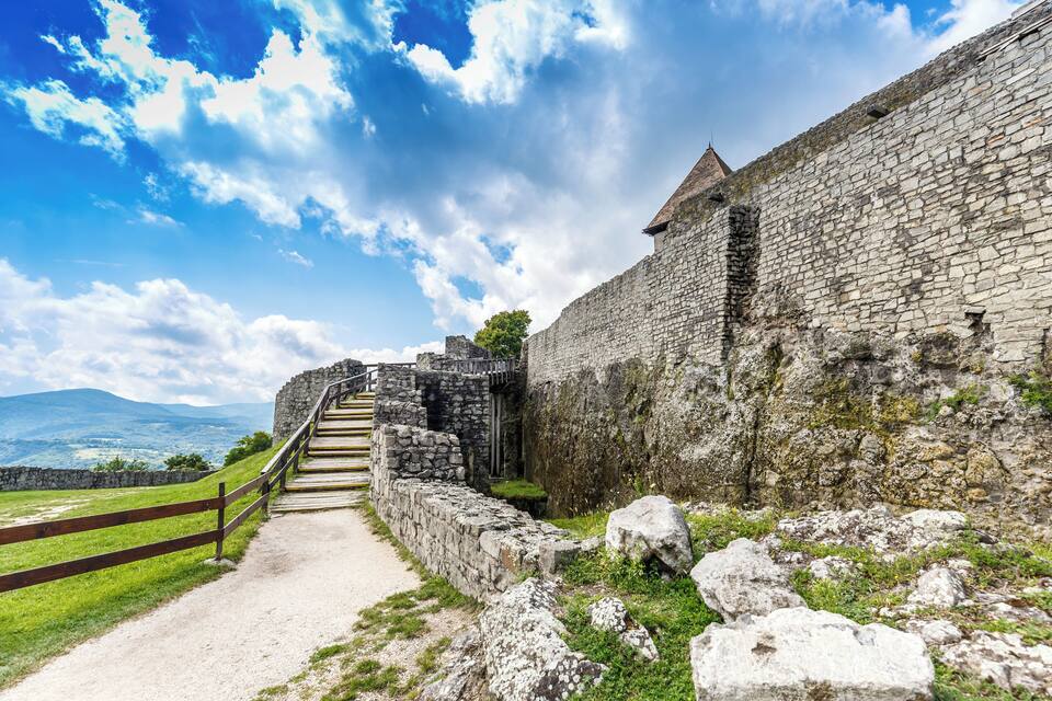 A stone staircase leading up to a historic stone wall with a clear sky and distant mountains.