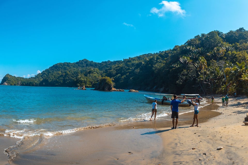 Une plage à l’eau d’un bleu cristallin, avec des bateaux et de luxuriantes collines verdoyantes.