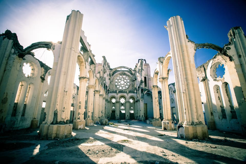 A ruined cathedral with tall columns and a large circular stained glass window.