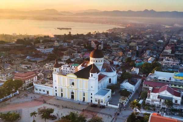A coastal cityscape with a prominent church featuring a large dome and bell tower, surrounded by dense urban buildings and a calm sea.