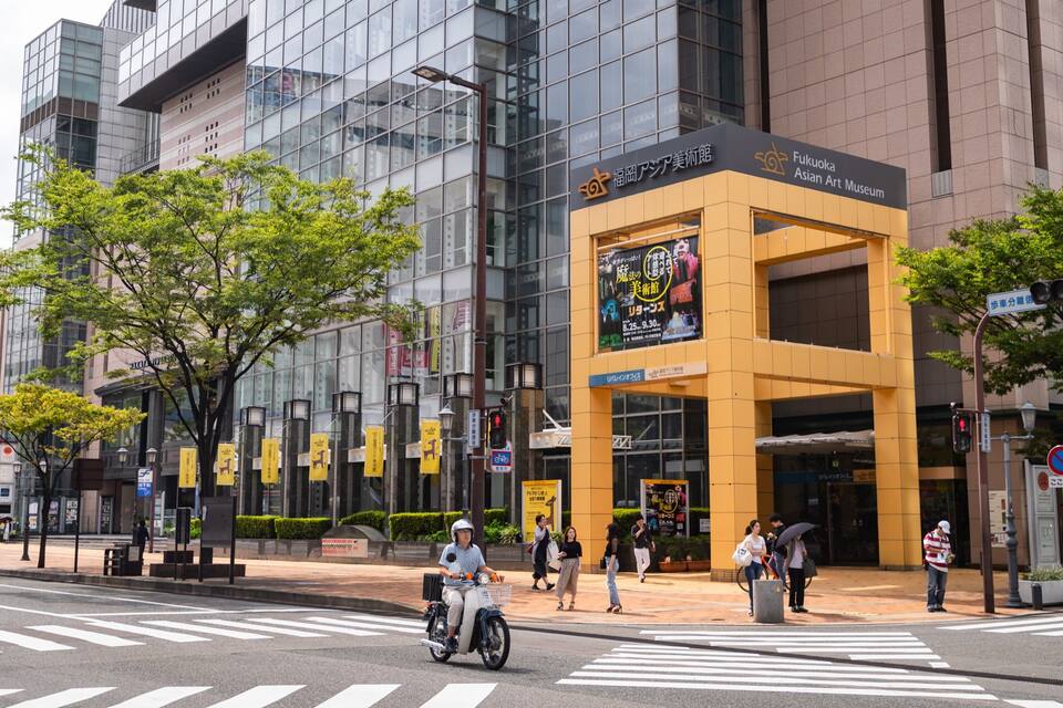 A modern urban street with a prominent building housing the Fukuoka Asian Art Museum.