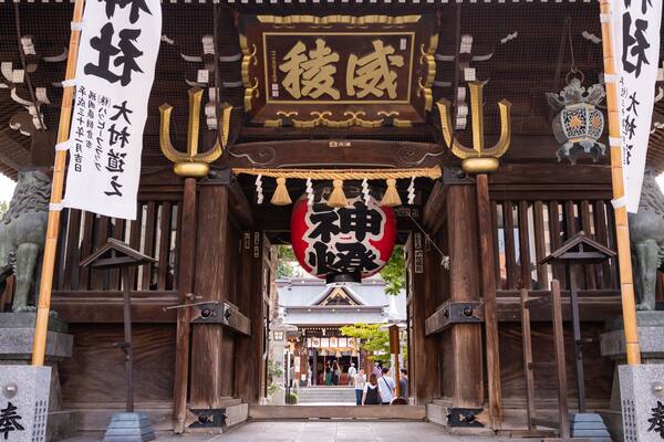 Une porte japonaise traditionnelle, avec de grands piliers en bois, une lanterne rouge et des caractères chinois.