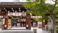 A traditional Japanese temple entrance with wooden architecture, a stone lantern, and cherry blossoms.