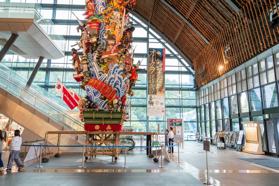 A large, colorful dragon sculpture in a modern building with glass walls and a wooden ceiling.