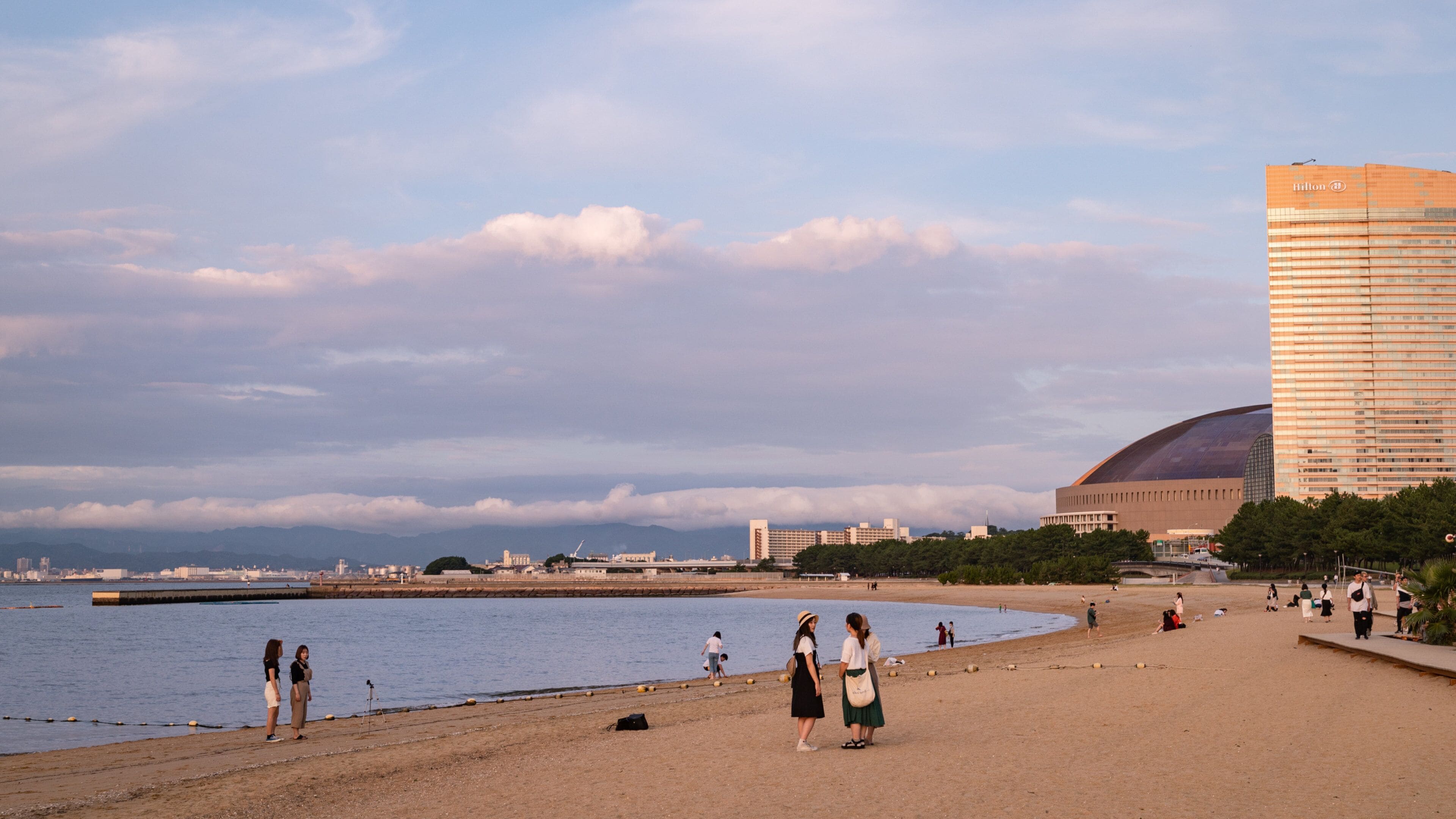 A beach with people, a large building, and mountains in the background.